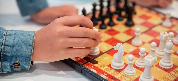 Close-up van een speler die tijdens een strategisch bordspel een schaakstuk verplaatst op een houten schaakbord.